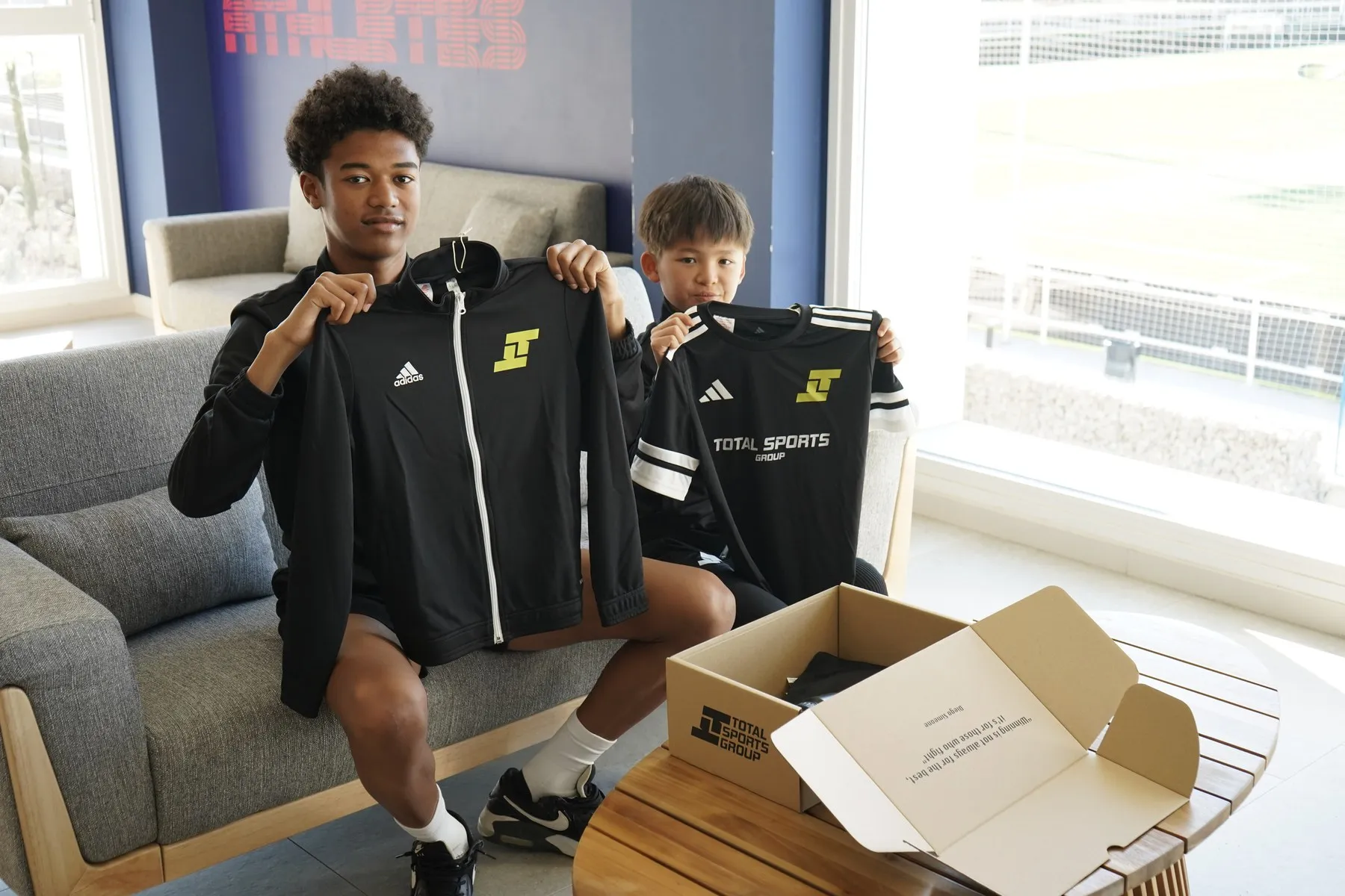 Two students holding up their Total Sports kit in the residence lounge