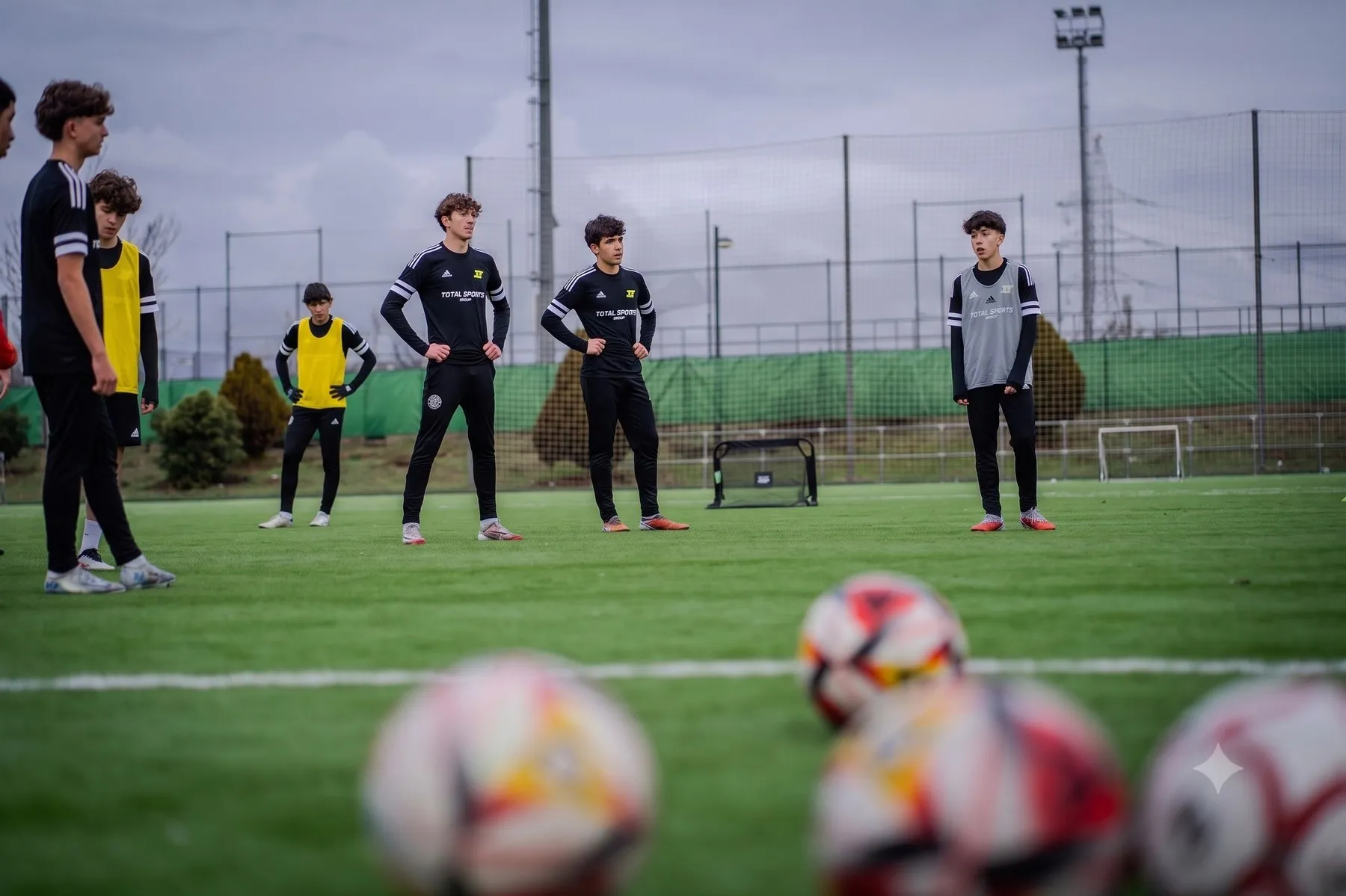 Players listening to instructions on the training pitch, balls in the foreground