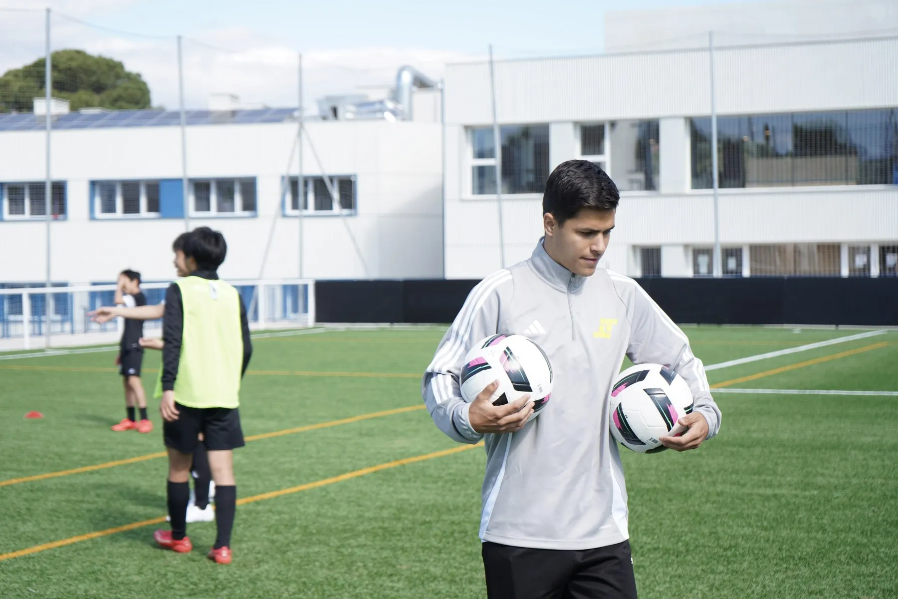 A coach carrying match balls onto the pitch during training